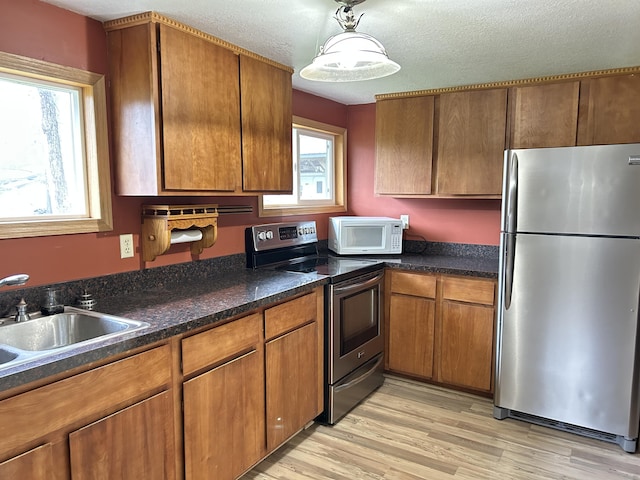 kitchen with brown cabinetry, light wood finished floors, a sink, dark stone counters, and appliances with stainless steel finishes
