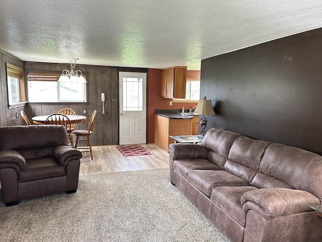 living room featuring an inviting chandelier, a textured ceiling, wood walls, and light wood-style floors