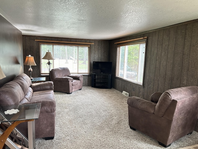carpeted living area with a healthy amount of sunlight, wood walls, visible vents, and a textured ceiling