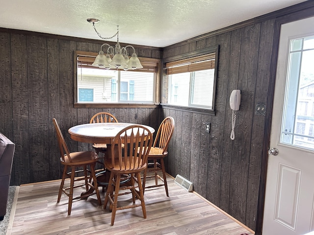 dining room with wooden walls, a chandelier, visible vents, and wood finished floors