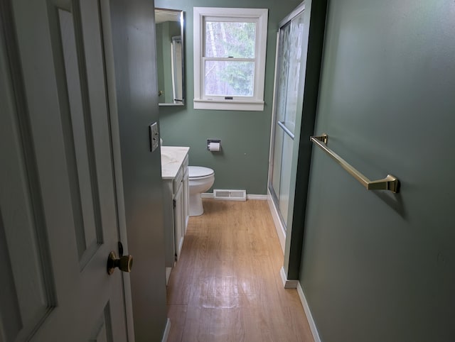 bathroom with wood finished floors, vanity, a shower stall, toilet, and baseboards