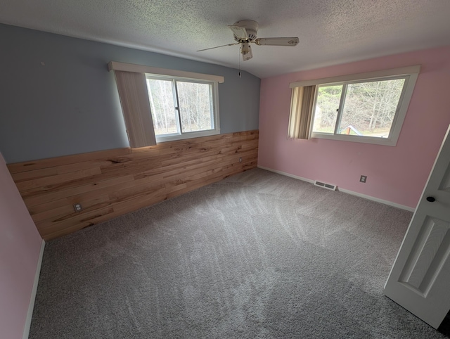 carpeted empty room with a ceiling fan, a textured ceiling, wood walls, and a wainscoted wall