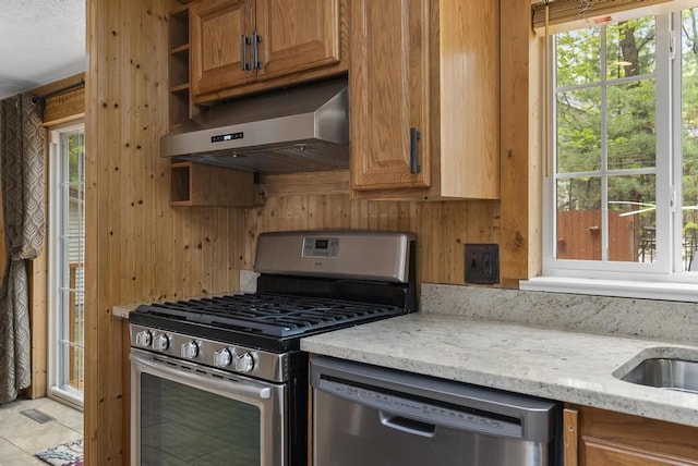 1505 Shawnee Dr, Indian River, MI 49749 - kitchen featuring appliances with stainless steel finishes, range hood, light stone countertops, brown cabinets, and wooden walls