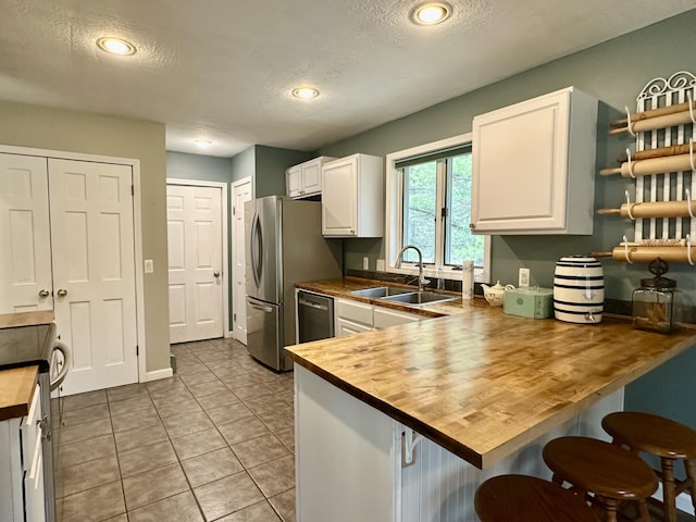 1243 Euclid Ave, Grayling, MI 49738 - kitchen featuring butcher block counters, a textured ceiling, a breakfast bar, white cabinets, and a sink