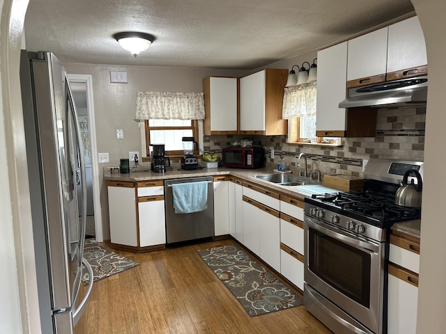 kitchen featuring appliances with stainless steel finishes, a sink, under cabinet range hood, white cabinetry, and a textured ceiling