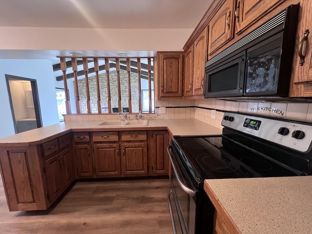 kitchen with stainless steel range with electric cooktop, black microwave, a sink, a peninsula, and dark wood-type flooring