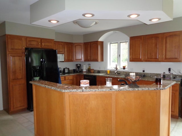 kitchen with a sink, stone countertops, black appliances, brown cabinets, and recessed lighting