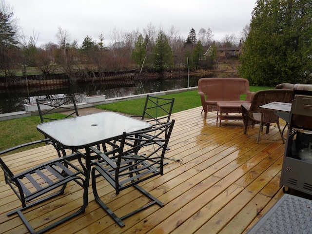 wooden terrace featuring outdoor dining space, a water view, and a yard