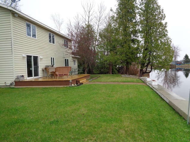 view of green lawn featuring a deck with water view