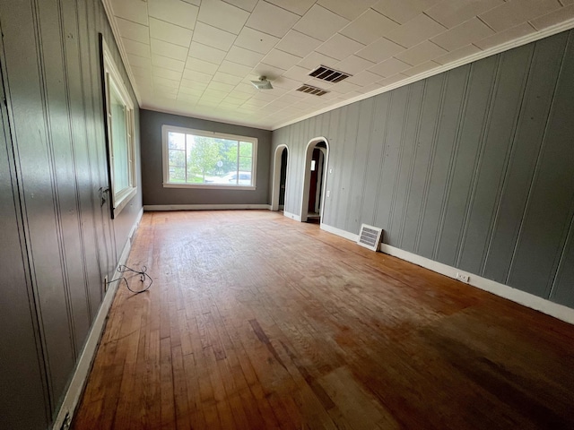 unfurnished living room with arched walkways, wood-type flooring, crown molding, wood walls, and baseboards