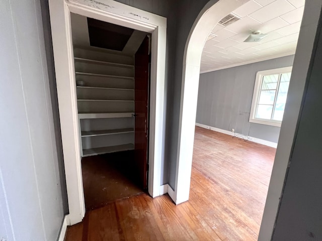 corridor featuring wood finished floors, baseboards, arched walkways, and ornamental molding