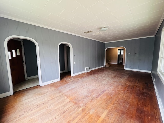 unfurnished living room featuring arched walkways, wood finished floors, and crown molding