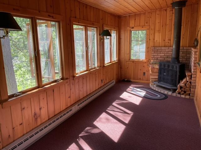 8842 Jackson Hole Trl, Grayling, MI 49738 - unfurnished sunroom featuring baseboard heating, wood walls, a wood stove, carpet floors, and wood ceiling