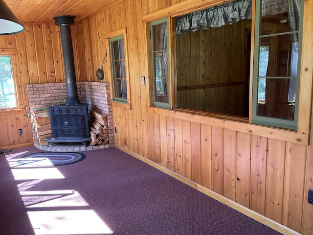 8842 Jackson Hole Trl, Grayling, MI 49738 - empty room featuring a wood stove, wood walls, carpet, and baseboards
