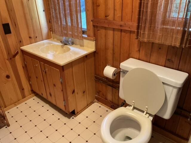 8842 Jackson Hole Trl, Grayling, MI 49738 - half bathroom featuring tile patterned floors, toilet, wood walls, and vanity