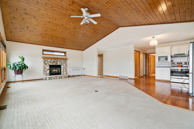 301 Hugh St, East Jordan, MI 49727 - unfurnished living room with baseboards, ceiling fan, carpet floors, a stone fireplace, and wooden ceiling