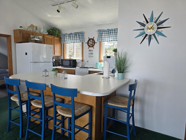 204 Broadway Rd, Houghton Lake, MI 48629 - kitchen with white appliances, light countertops, track lighting, brown cabinetry, and a breakfast bar area