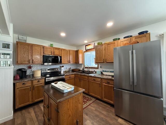kitchen with appliances with stainless steel finishes, dark countertops, dark wood finished floors, brown cabinets, and recessed lighting