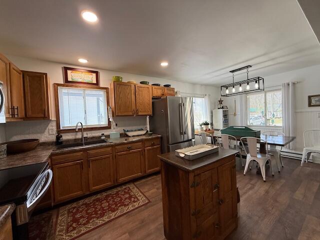 kitchen featuring a sink, freestanding refrigerator, brown cabinetry, dark countertops, and range with electric stovetop