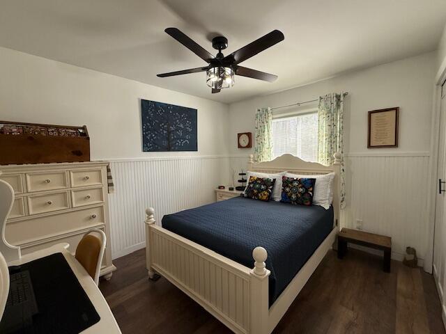 bedroom with a wainscoted wall, dark wood-type flooring, and ceiling fan