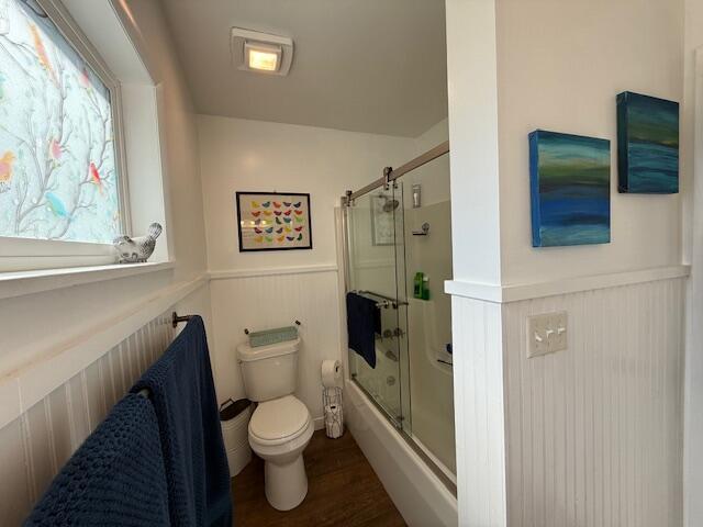 full bathroom featuring wainscoting, toilet, shower / bath combination with glass door, and wood finished floors