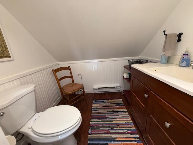 half bathroom with a baseboard heating unit, wainscoting, toilet, wood finished floors, and vanity