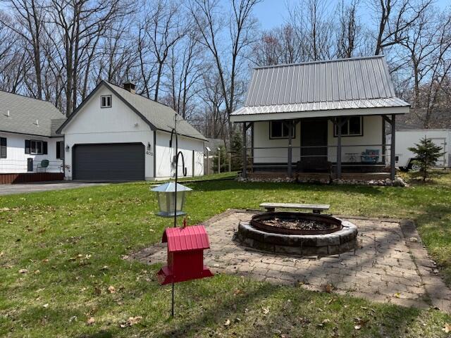 view of grassy yard with a porch, a fire pit, a garage, and asphalt driveway
