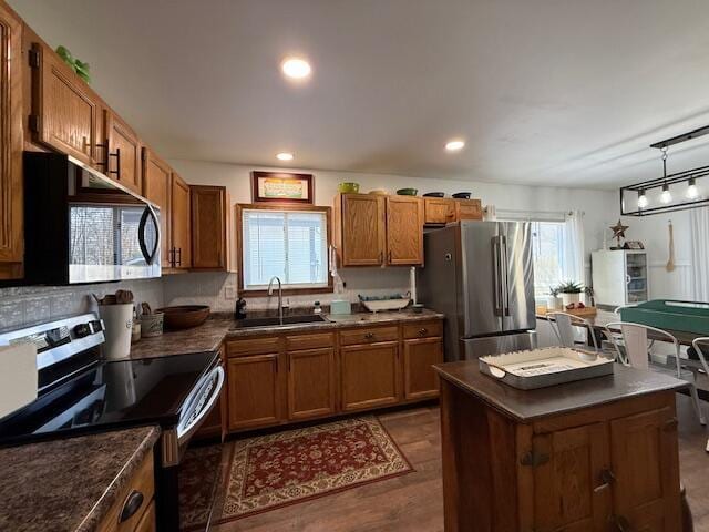 kitchen featuring appliances with stainless steel finishes, a sink, brown cabinets, dark countertops, and dark wood-type flooring