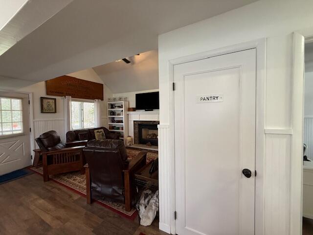 office featuring wood finished floors, a fireplace, wainscoting, vaulted ceiling, and a decorative wall