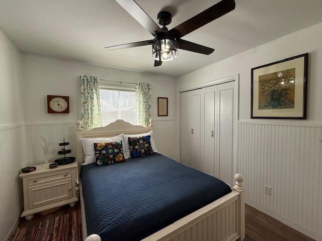 bedroom featuring dark wood-type flooring, a wainscoted wall, a closet, and ceiling fan