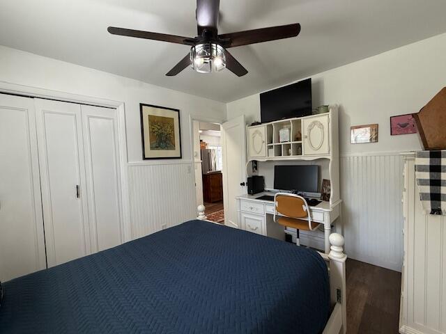 bedroom featuring wood finished floors, a wainscoted wall, a closet, ceiling fan, and a desk