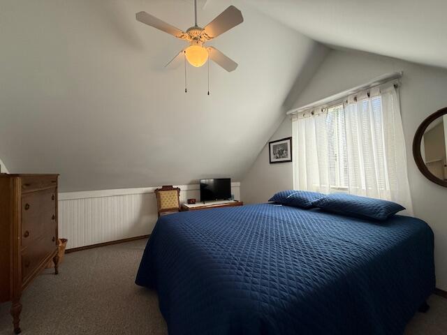 bedroom with vaulted ceiling, carpet flooring, wainscoting, and a ceiling fan