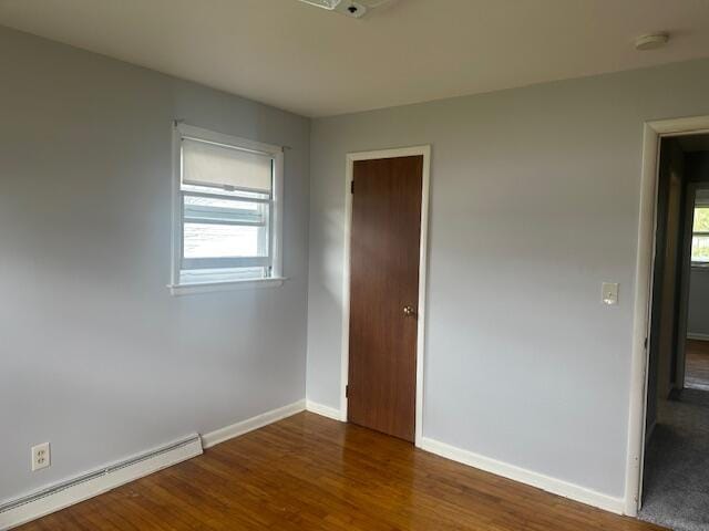 unfurnished room with baseboard heating, baseboards, and wood finished floors