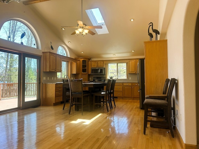 dining area with a skylight, a ceiling fan, light wood-style flooring, recessed lighting, and high vaulted ceiling