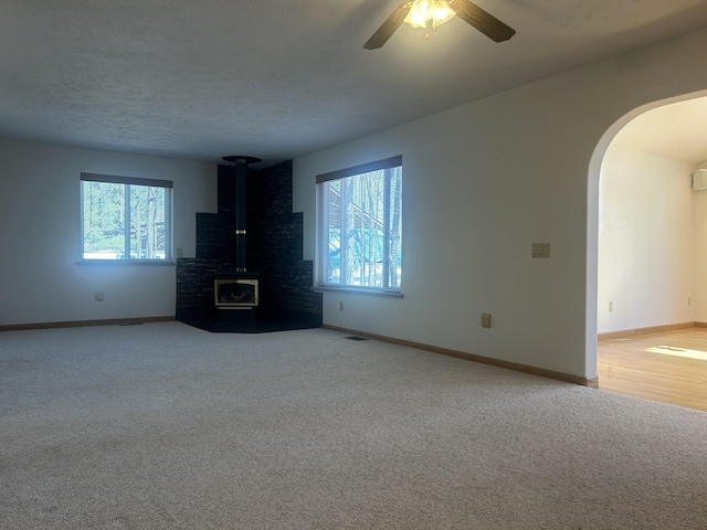 unfurnished living room with arched walkways, carpet, baseboards, and a wood stove
