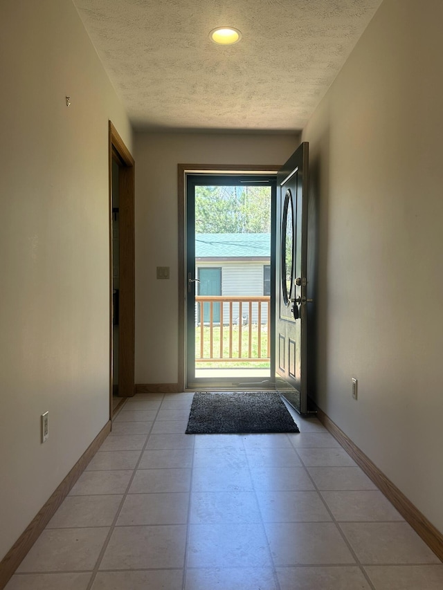 doorway to outside featuring a textured ceiling, baseboards, and light tile patterned floors