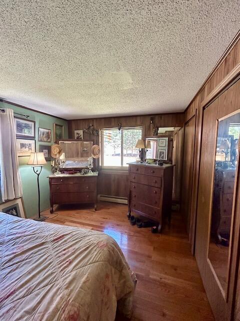 2165 E Cherry Creek Rd, Fairview, MI 48621 - bedroom featuring a textured ceiling, a baseboard heating unit, wood finished floors, and wood walls