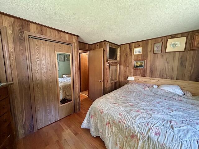 2165 E Cherry Creek Rd, Fairview, MI 48621 - bedroom featuring wooden walls, wood finished floors, and a textured ceiling