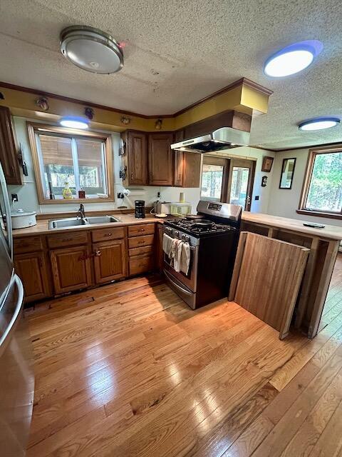 2165 E Cherry Creek Rd, Fairview, MI 48621 - kitchen featuring stainless steel gas stove, wall chimney exhaust hood, light wood-style flooring, a textured ceiling, and a sink