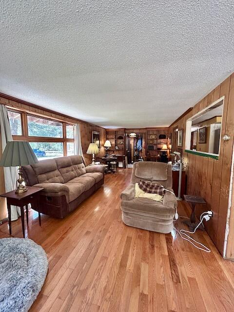 2165 E Cherry Creek Rd, Fairview, MI 48621 - living room with a textured ceiling, light wood-style flooring, and wooden walls