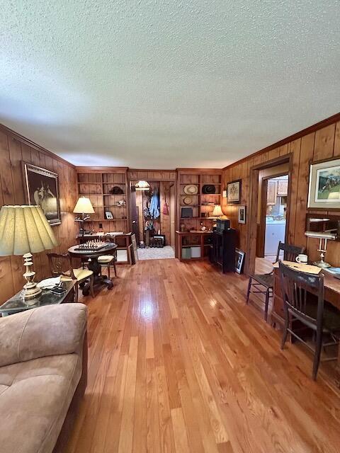 2165 E Cherry Creek Rd, Fairview, MI 48621 - living area featuring wooden walls, a textured ceiling, light wood finished floors, crown molding, and washer / dryer