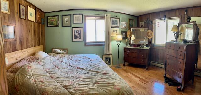2165 E Cherry Creek Rd, Fairview, MI 48621 - bedroom featuring baseboard heating, multiple windows, light wood-style floors, wooden walls, and ornamental molding