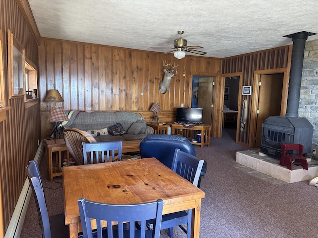 dining area featuring a wood stove, ceiling fan, carpet, wood walls, and a textured ceiling