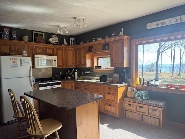 kitchen featuring white appliances, carpet, a kitchen island, dark countertops, and a kitchen breakfast bar