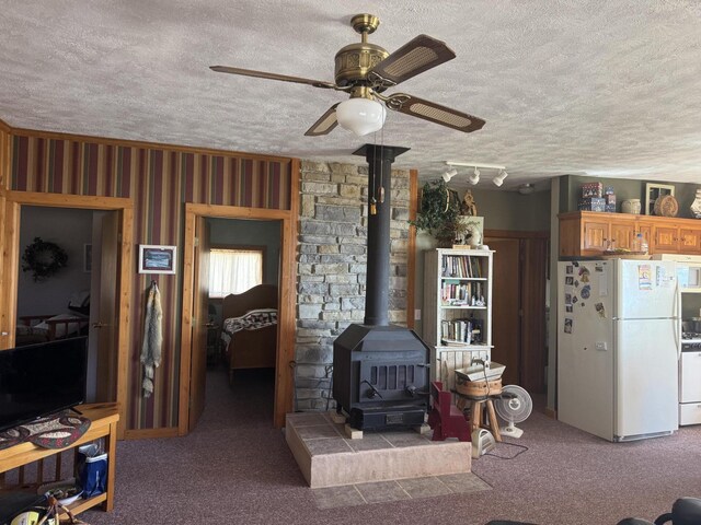 living area with a textured ceiling, carpet flooring, a wood stove, and ceiling fan