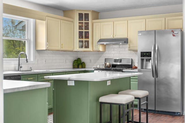 201 Country Ct, Houghton Lake, MI 48629 - kitchen with stainless steel appliances, under cabinet range hood, cream cabinetry, light countertops, and a kitchen island