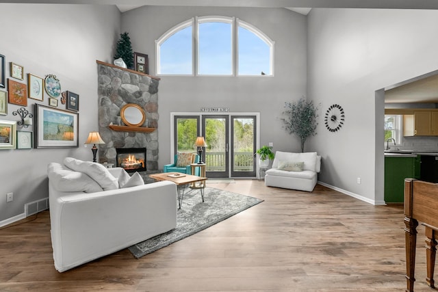 201 Country Ct, Houghton Lake, MI 48629 - living area with healthy amount of natural light, a stone fireplace, a towering ceiling, baseboards, and wood finished floors