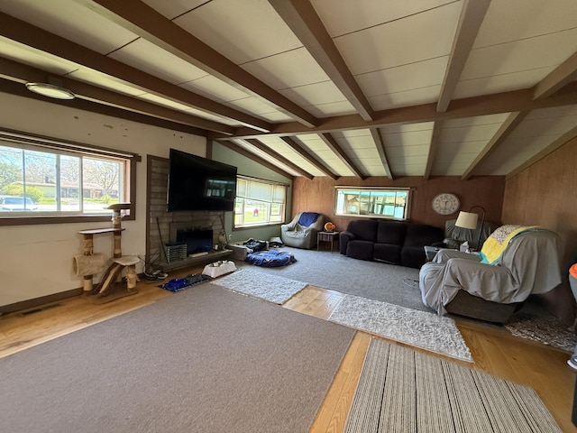 living area with a stone fireplace, wood finished floors, and wooden walls