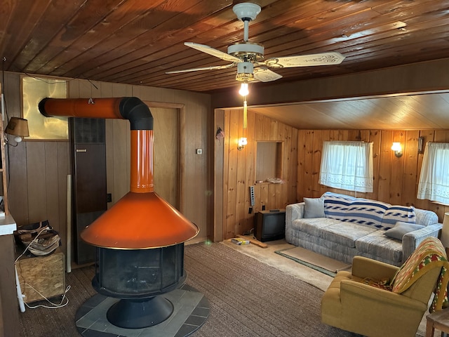carpeted bedroom with a wood stove, wood walls, wooden ceiling, and ceiling fan