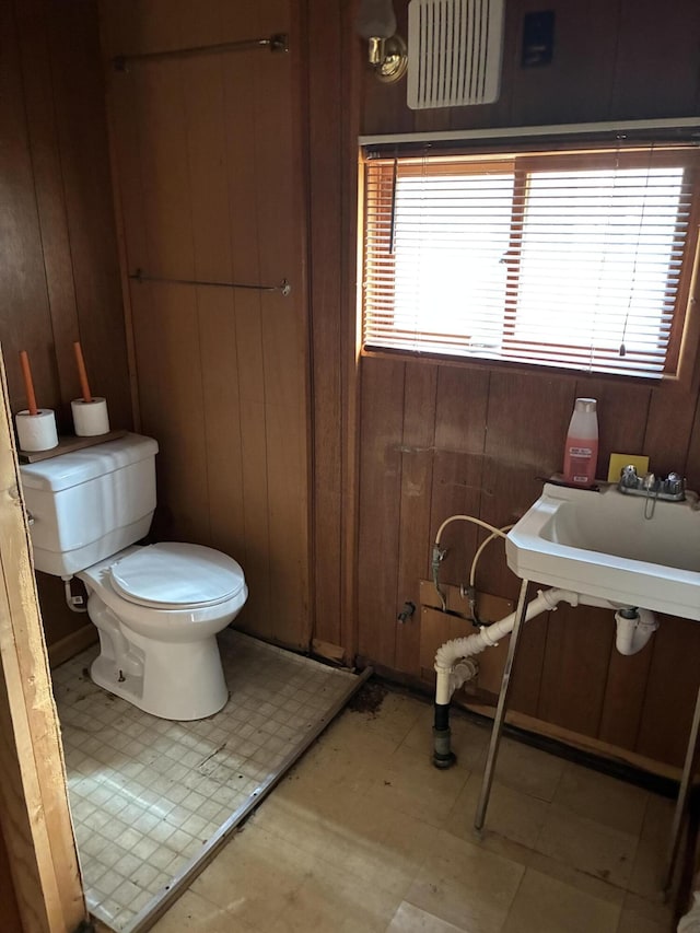 bathroom featuring toilet, wooden walls, tile patterned floors, and a sink